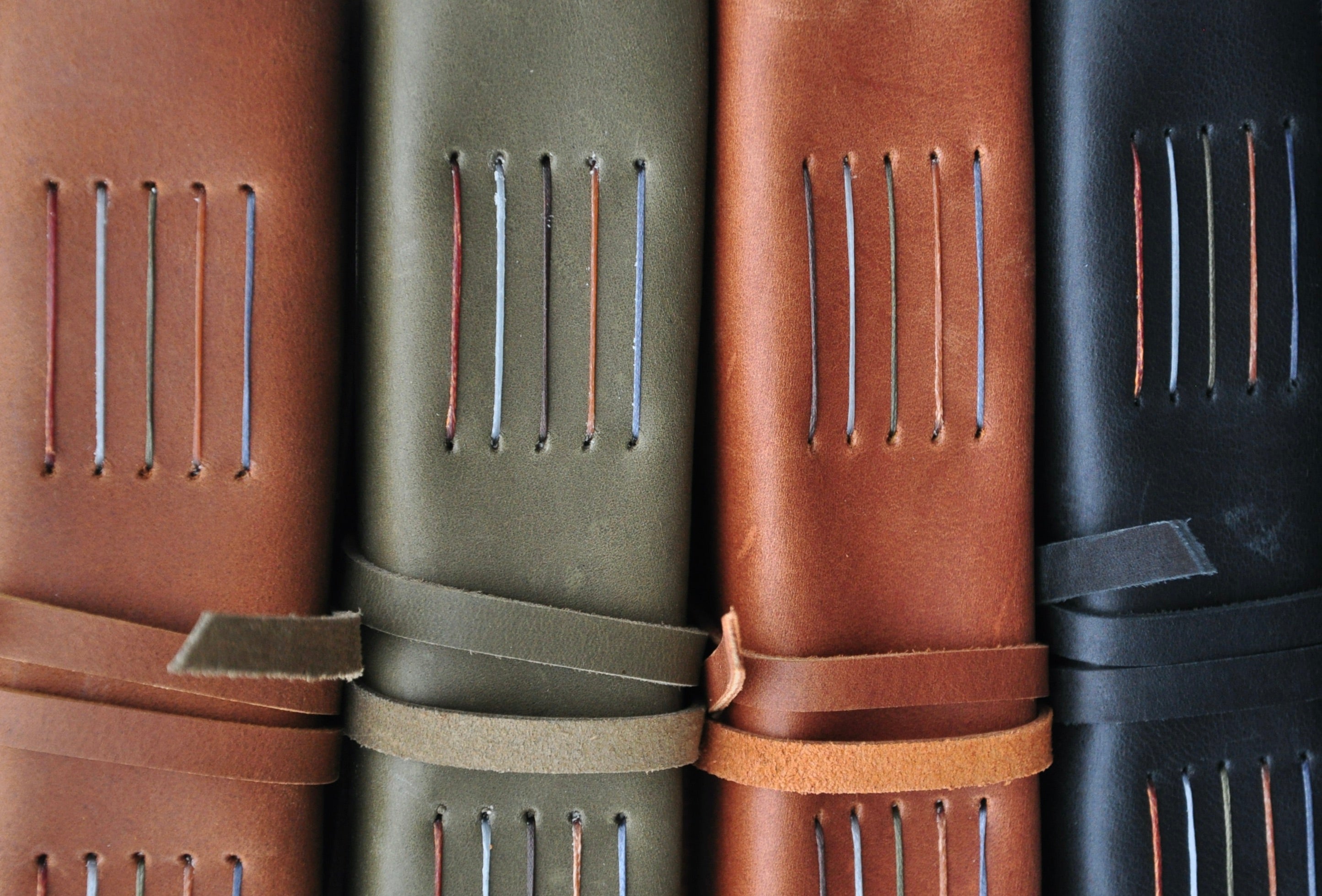 Hand-bound leather journals in black, rust, olive, and brown